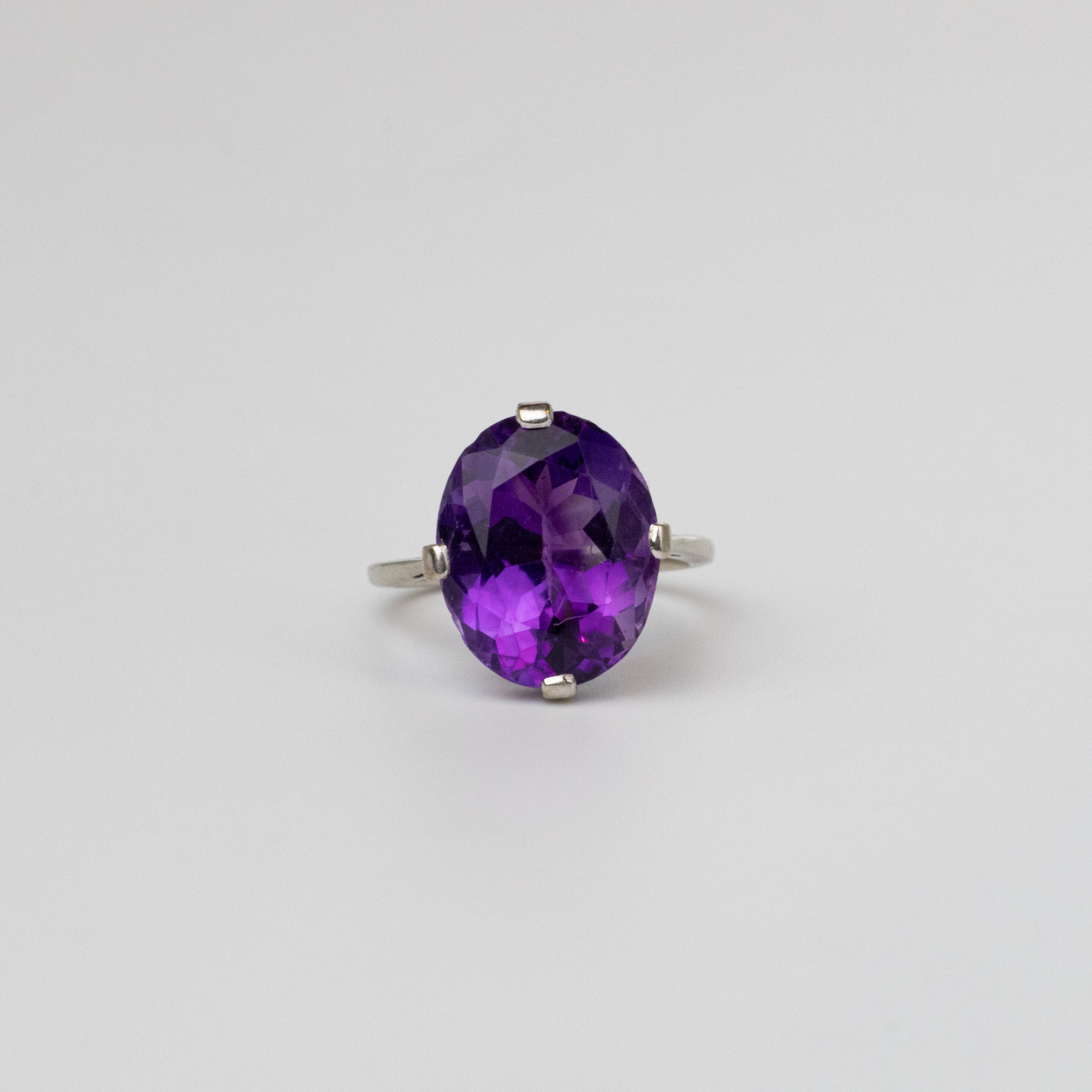 An oval-cut purple gemstone ring set in a white gold band, photographed against a plain light gray background.