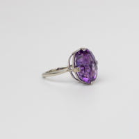A white gold ring featuring a large, oval-cut amethyst gemstone in a prong setting, photographed on a clean, light gray background.
